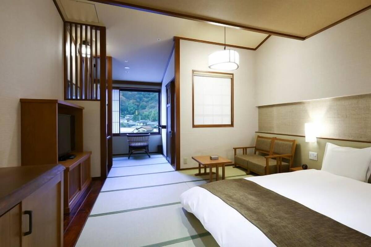 A hotel room with a bed, a desk, a chair, a television, and a view of a balcony.