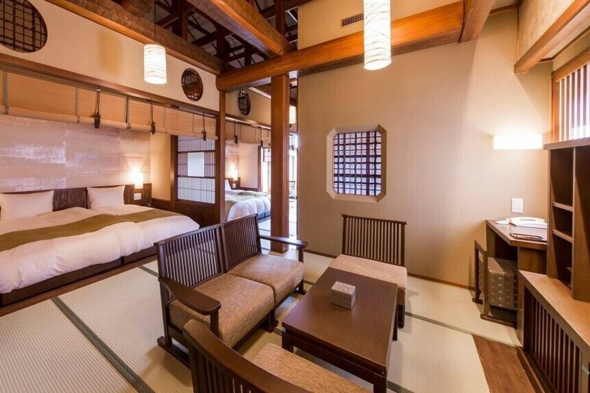 A traditional Japanese-style room with tatami flooring, a low wooden bed, a sofa, a table, and a small desk.