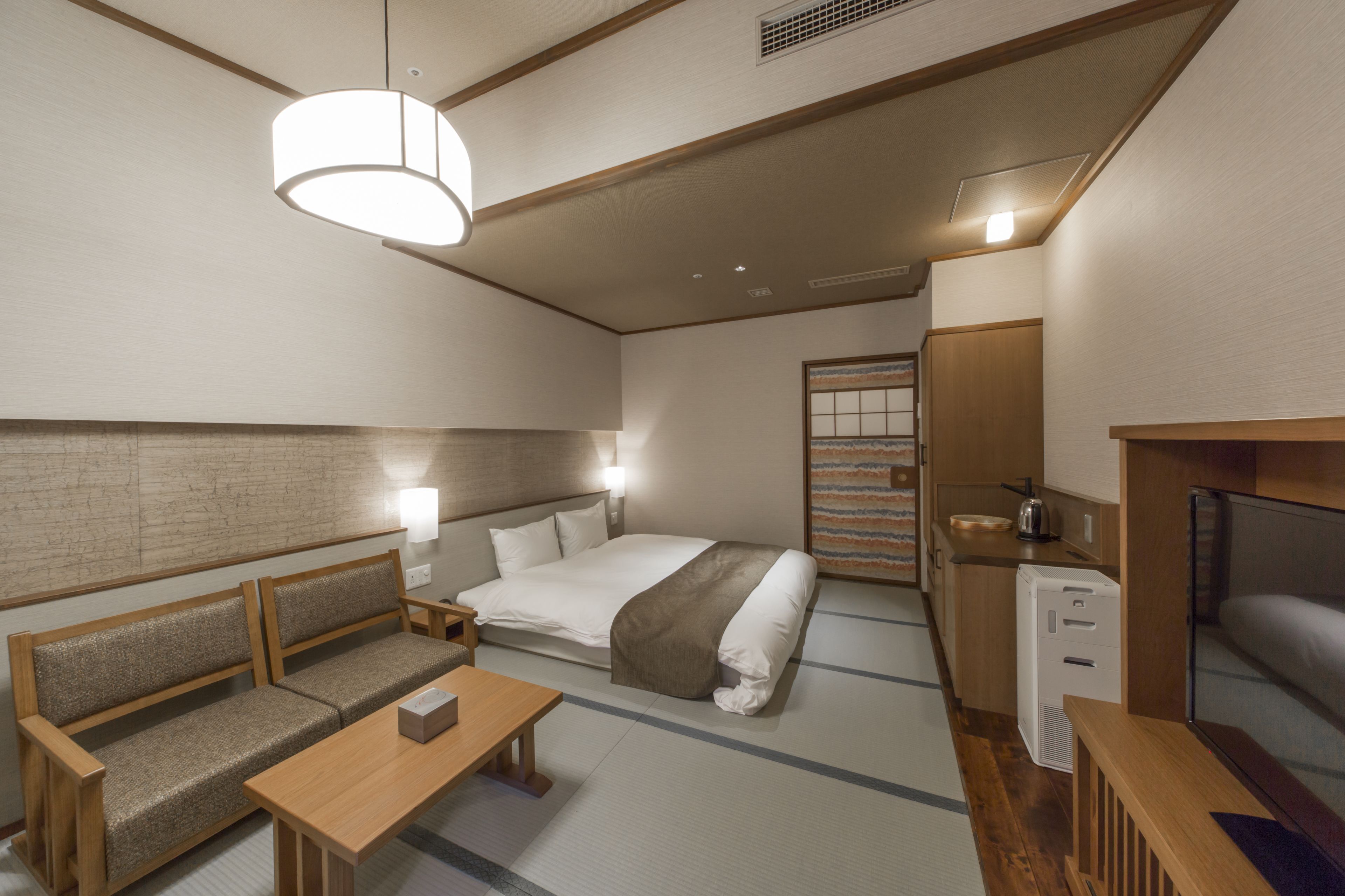 Una habitación de hotel compacta con cama, sofá, mesita de noche y una pequeña kitchenette.