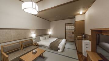 Una habitación de hotel compacta con cama, sofá, mesita de noche y una pequeña kitchenette.