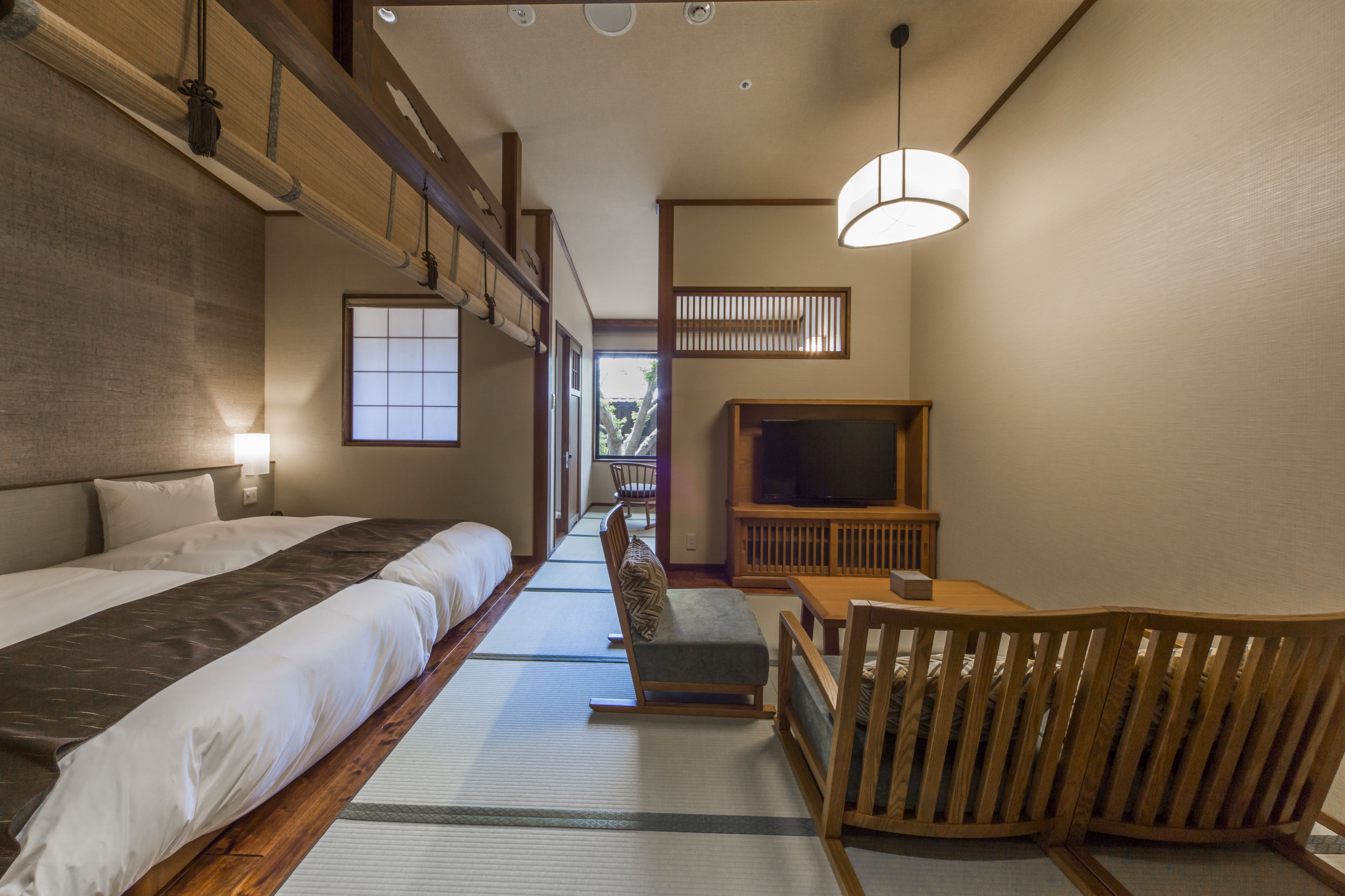 Una habitación de estilo japonés tradicional con suelo de tatami, una cama baja de madera, televisión y un pequeño rincón de estar.