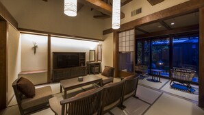 A traditional Japanese-style living room with tatami flooring, low wooden furniture, and a television. - Inisienoyado Keiunn (Izumo)