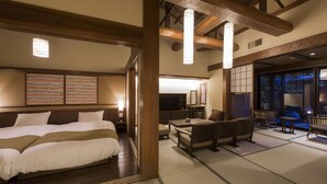 A traditional Japanese-style hotel room with tatami flooring, a large bed, a sitting area with low tables and benches, and a view of the outside. - Inisienoyado Keiunn (Izumo)