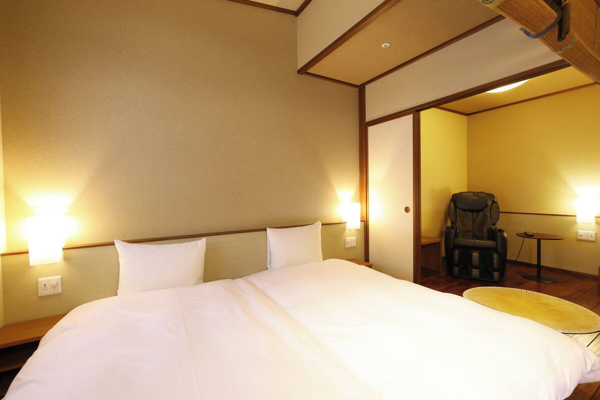 A hotel room with a large bed, two wall-mounted lights, a massage chair, and a small table.