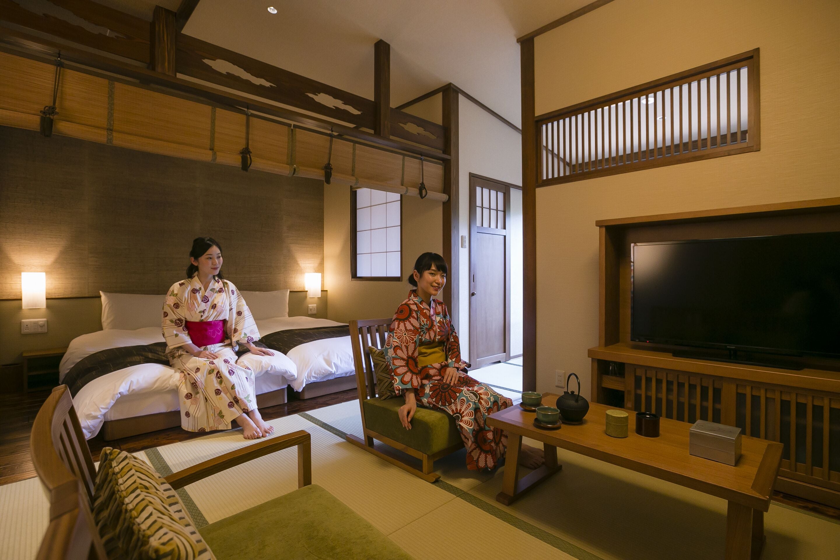 Une pièce de style japonais traditionnel, avec un sol recouvert de tatamis, une petite table en bois et un service à thé, ainsi qu’un grand écran de télévision.
