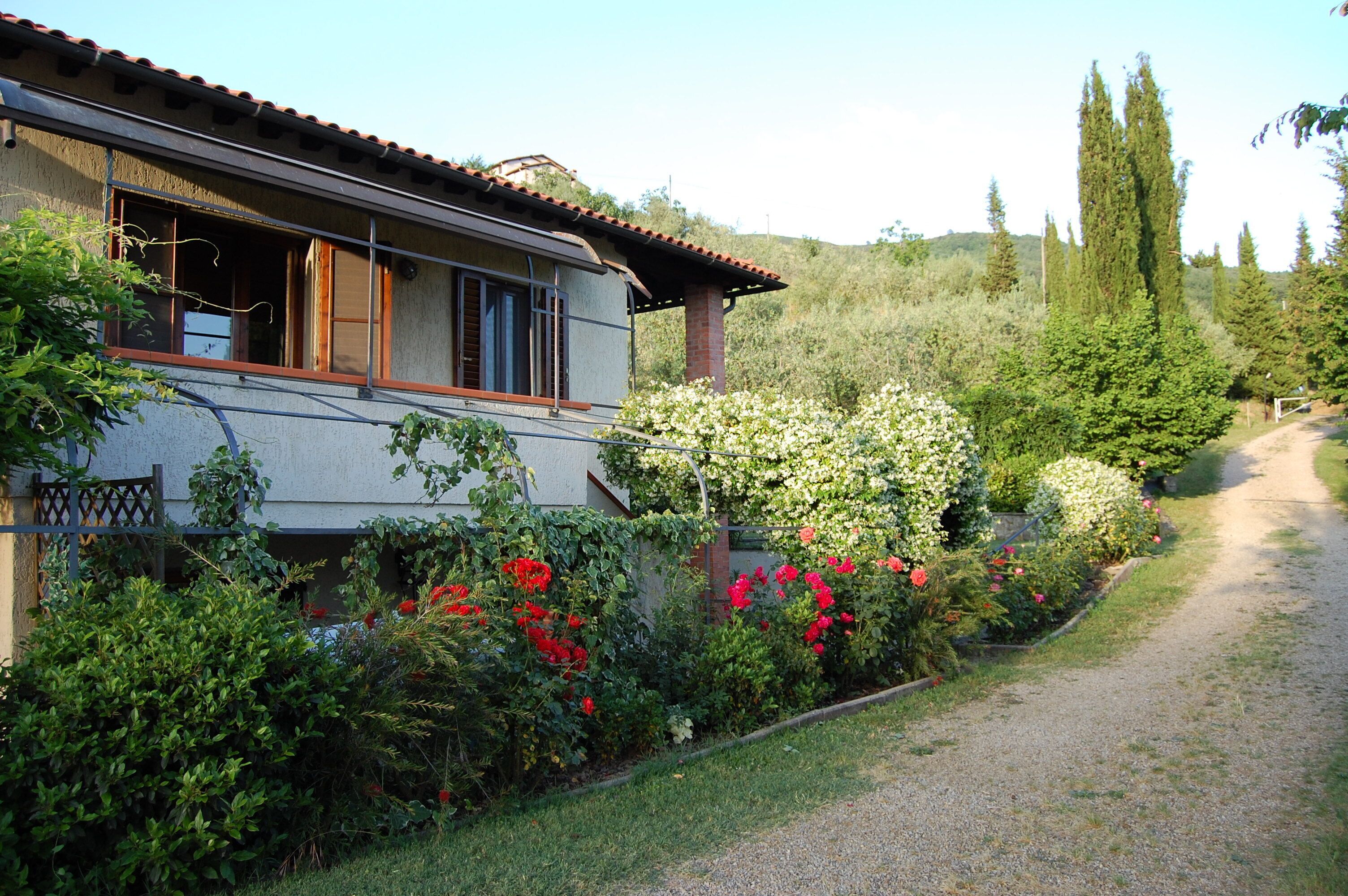 Una casa con jardín, un camino de grava y una colina al fondo.