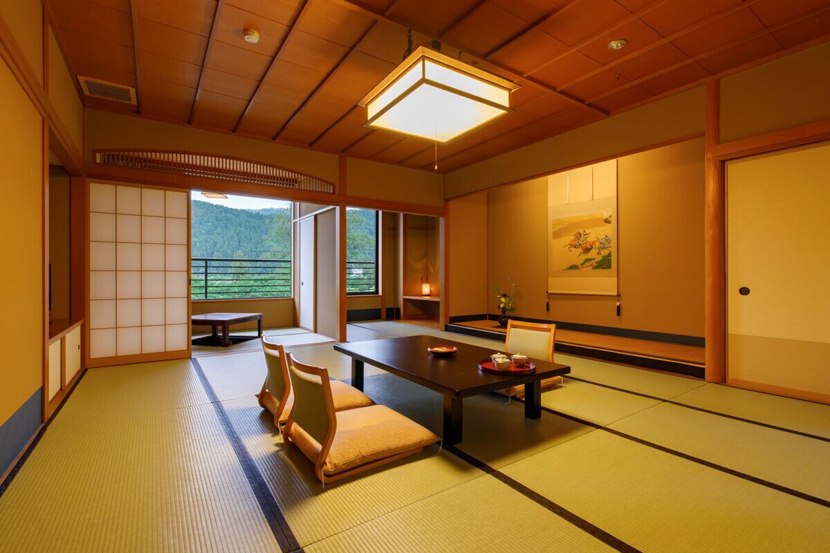 Una habitación japonesa tradicional con suelo de tatami, una mesa baja, cojines, puertas correderas y vistas al verdor.