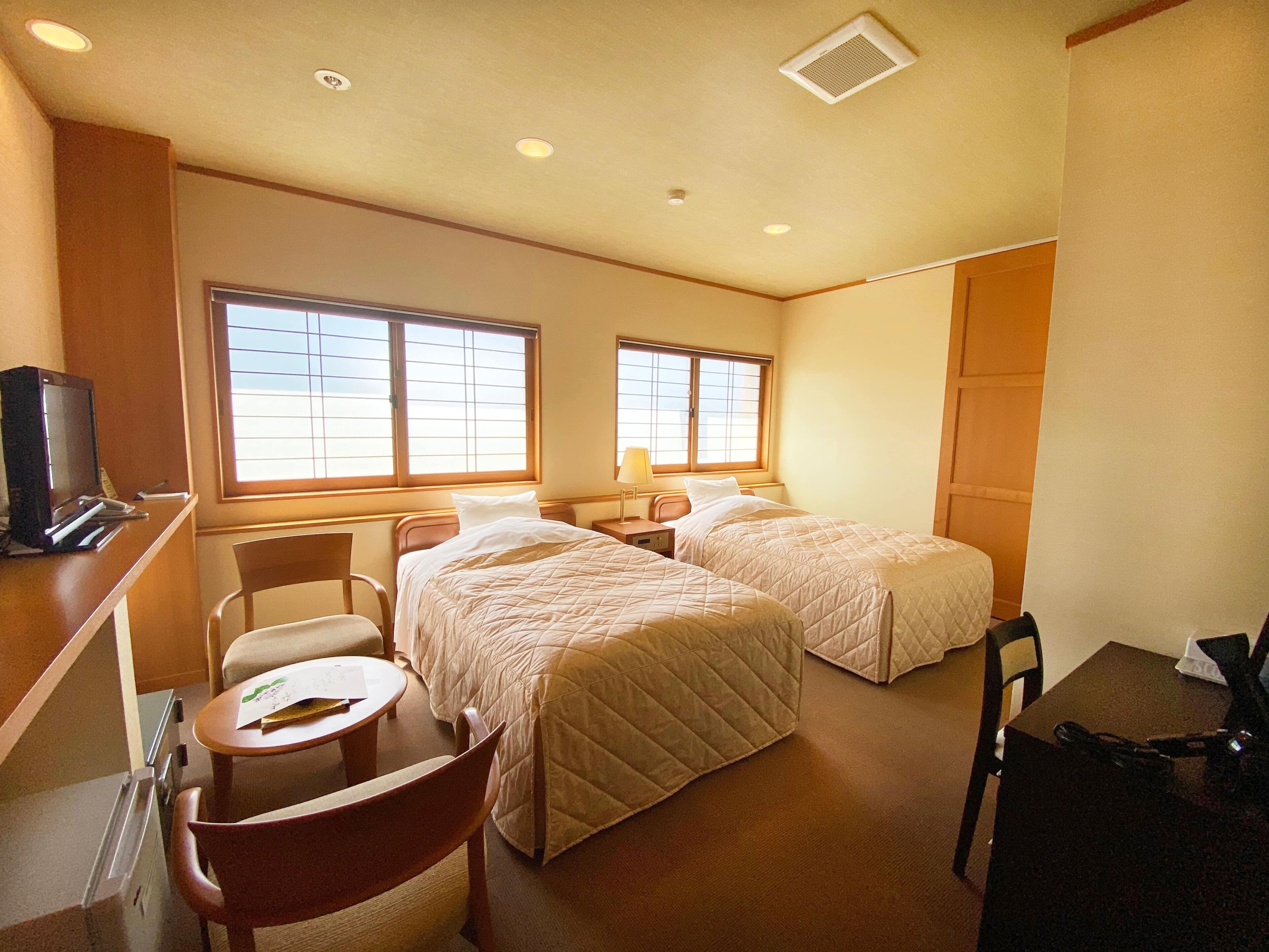 Una habitación de hotel con dos camas, un escritorio con ordenador, una silla y una mesita.