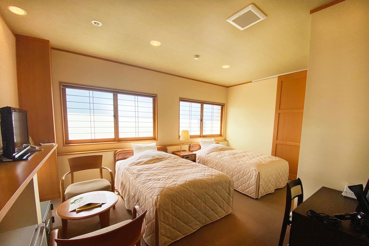 A hotel room with two beds, a desk with a computer, a chair, and a small table.