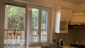 Una cocina con fregadero, estufa y armarios. Hay dos ventanas con cortinas.