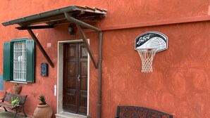 Un edificio con un aro de baloncesto, un banco de madera y una puerta con contraventanas verdes.