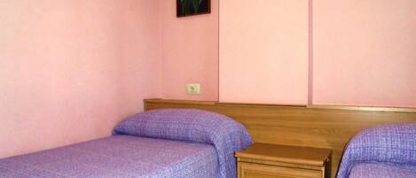 A bedroom with two single beds, a wooden nightstand, and a wall-mounted light switch.