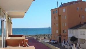 Un balcón con vista al mar, un edificio con varias ventanas y un coche aparcado.
