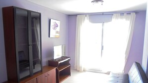 Una sala de estar con sofá, televisión sobre un mueble bajo, aparador y ventana con cortinas.