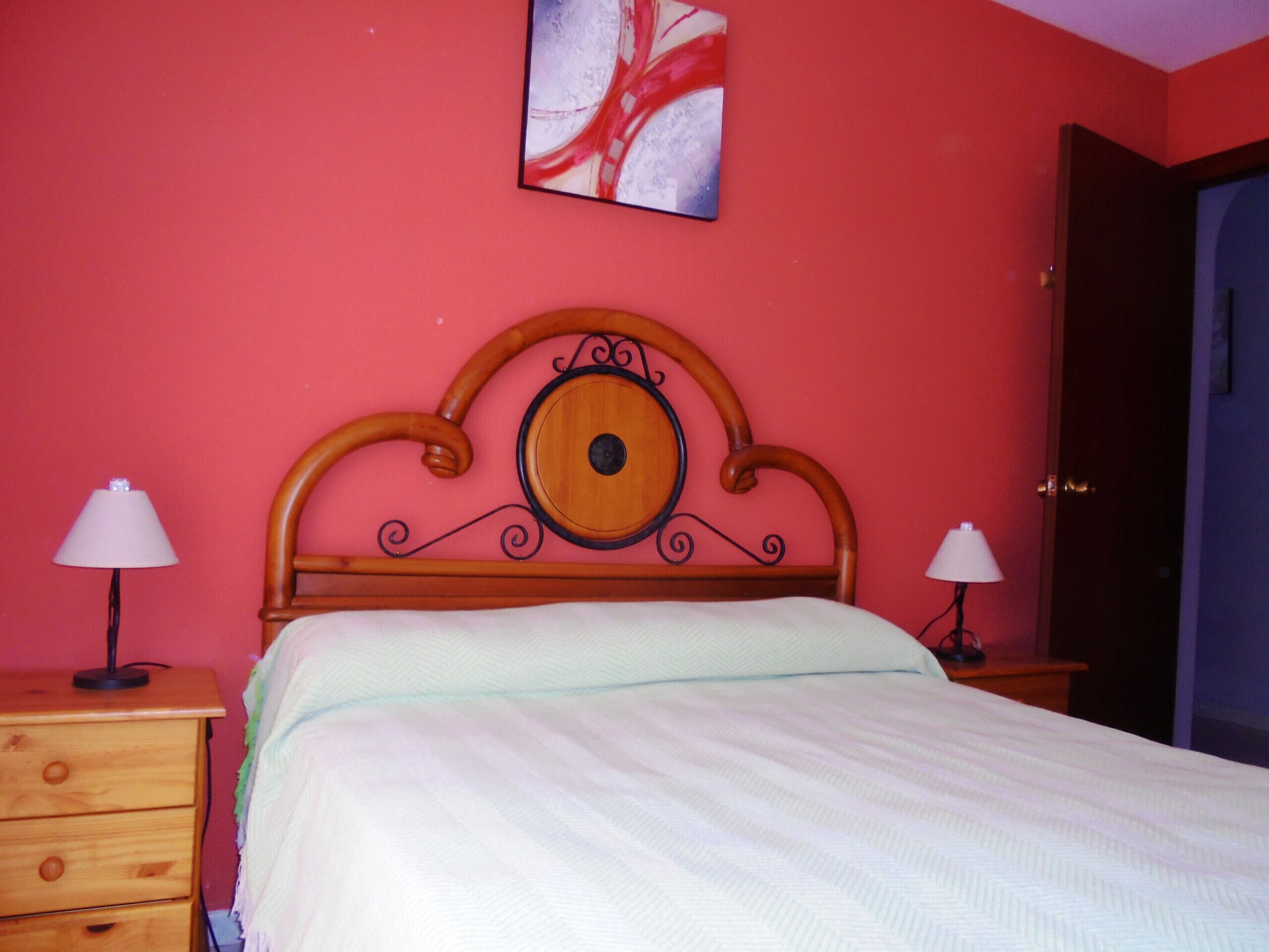Une chambre à coucher avec une tête de lit en bois, deux tables de chevet avec des lampes, une commode en bois et un tableau accroché au mur.