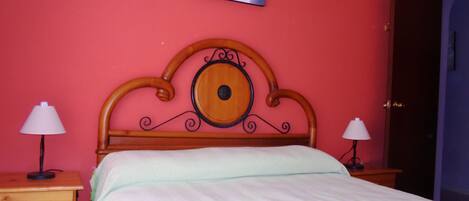 Une chambre à coucher avec une tête de lit en bois, deux tables de chevet avec des lampes, une commode en bois et un tableau accroché au mur.