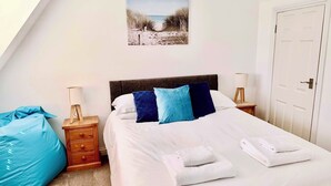 Ein Schlafzimmer mit Bett, Kissen, Nachttisch, Lampe, einer Tür und einem Bild an der Wand.