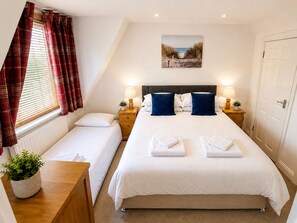 Een hotelkamer met een groot bed, twee nachtkastjes met lampen, een raam met gordijnen, een kleine plant en een schilderij aan de muur.