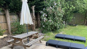 Ein Holzpicknicktisch mit Baldachin, zwei schwarze gepolsterte Bänke und ein Garten mit blühenden Büschen.