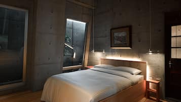 Een slaapkamer met een groot bed, een nachtkastje, een wandlamp en een raam met jaloezieën.