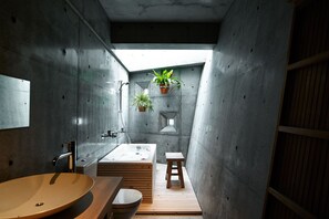 A modern bathroom with a large sink, a bathtub, and a small stool. There are two potted plants hanging from the ceiling.