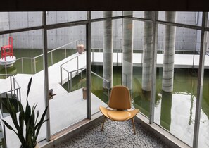 A modern interior with a large glass window overlooking a water feature and a seating area with a chair.