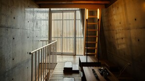 A modern interior with a concrete wall, a wooden staircase, and a view through a large window. - Mao House (Tainan)