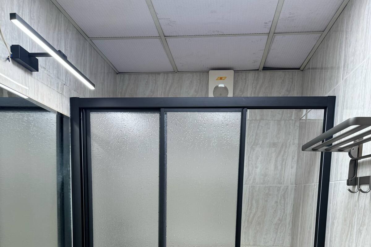 A bathroom with a white sink, frosted glass shower door, and tiled walls.