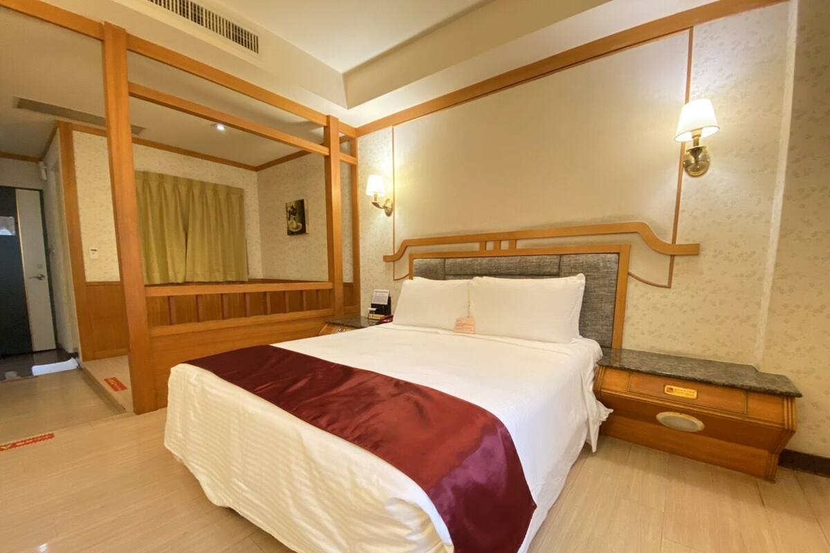 A hotel room with a large bed, wooden headboard, two bedside tables, and a nightstand.