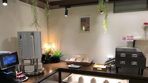 Un coin café équipé d’une machine à café, d’un présentoir rempli de gobelets en papier et d’un panier de pain.