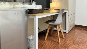 Une pièce de taille modeste, équipée d’un bureau, d’une chaise et d’un petit réfrigérateur.