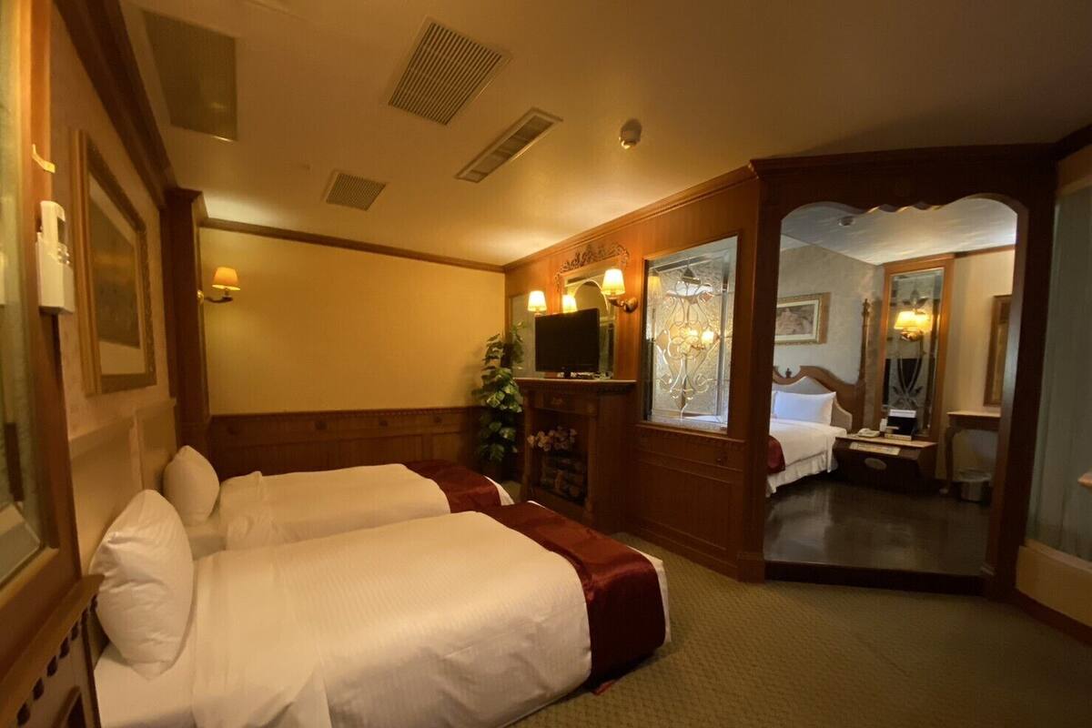 A hotel room with two beds, a television, a mirror, and a small desk with a lamp.