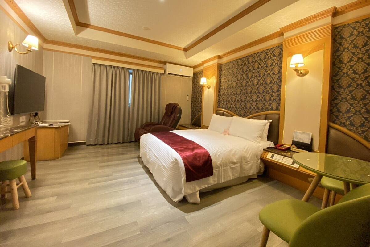 A hotel room with a bed, a desk with a computer, a chair, and a TV.