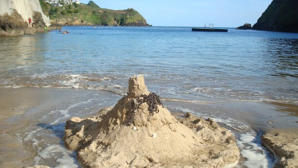 Una playa arenosa con una gran formación de arena en primer plano y un barco al fondo.