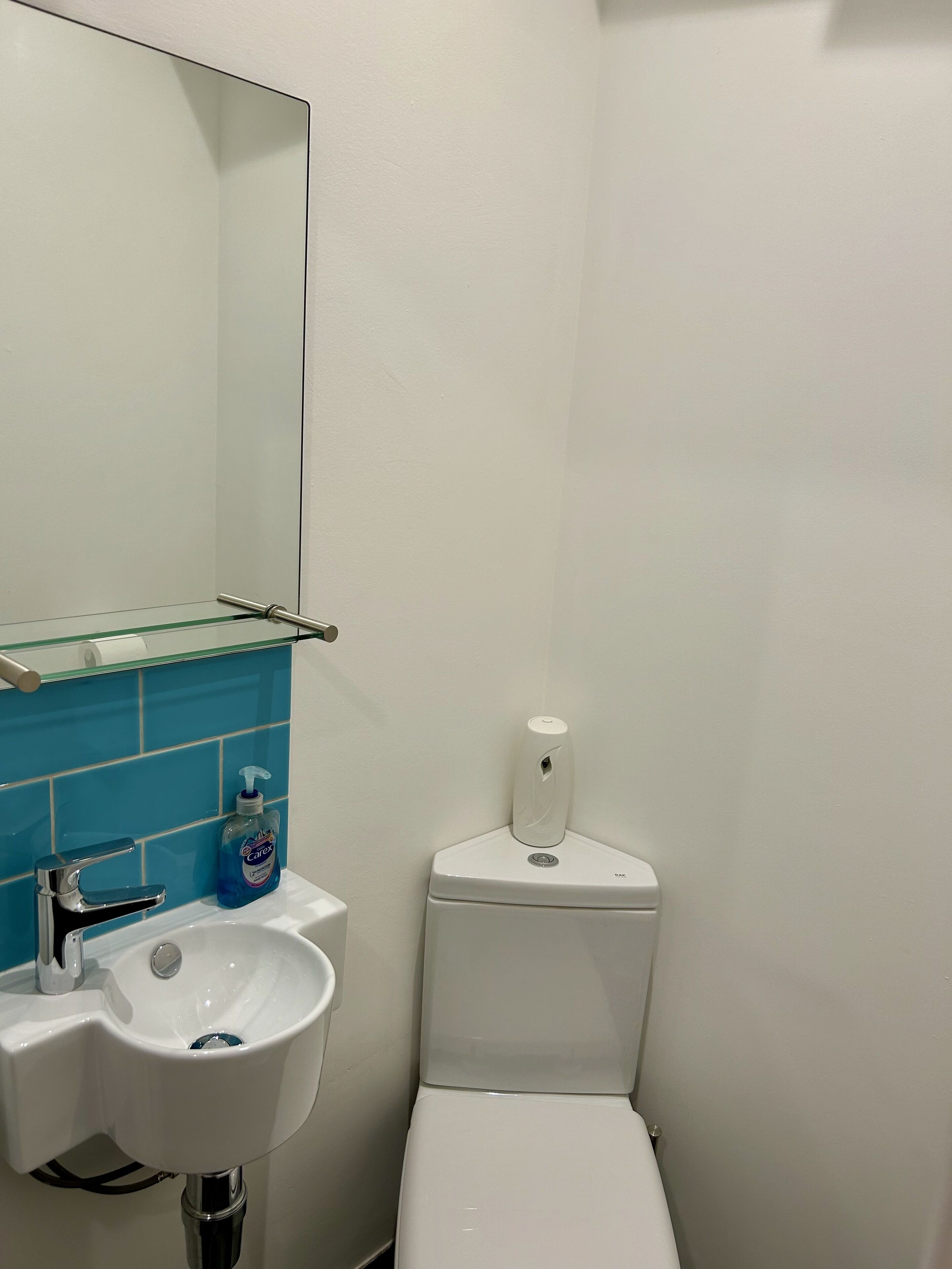 Un baño con un lavamanos blanco, un espejo, un dispensador de jabón azul y un inodoro.