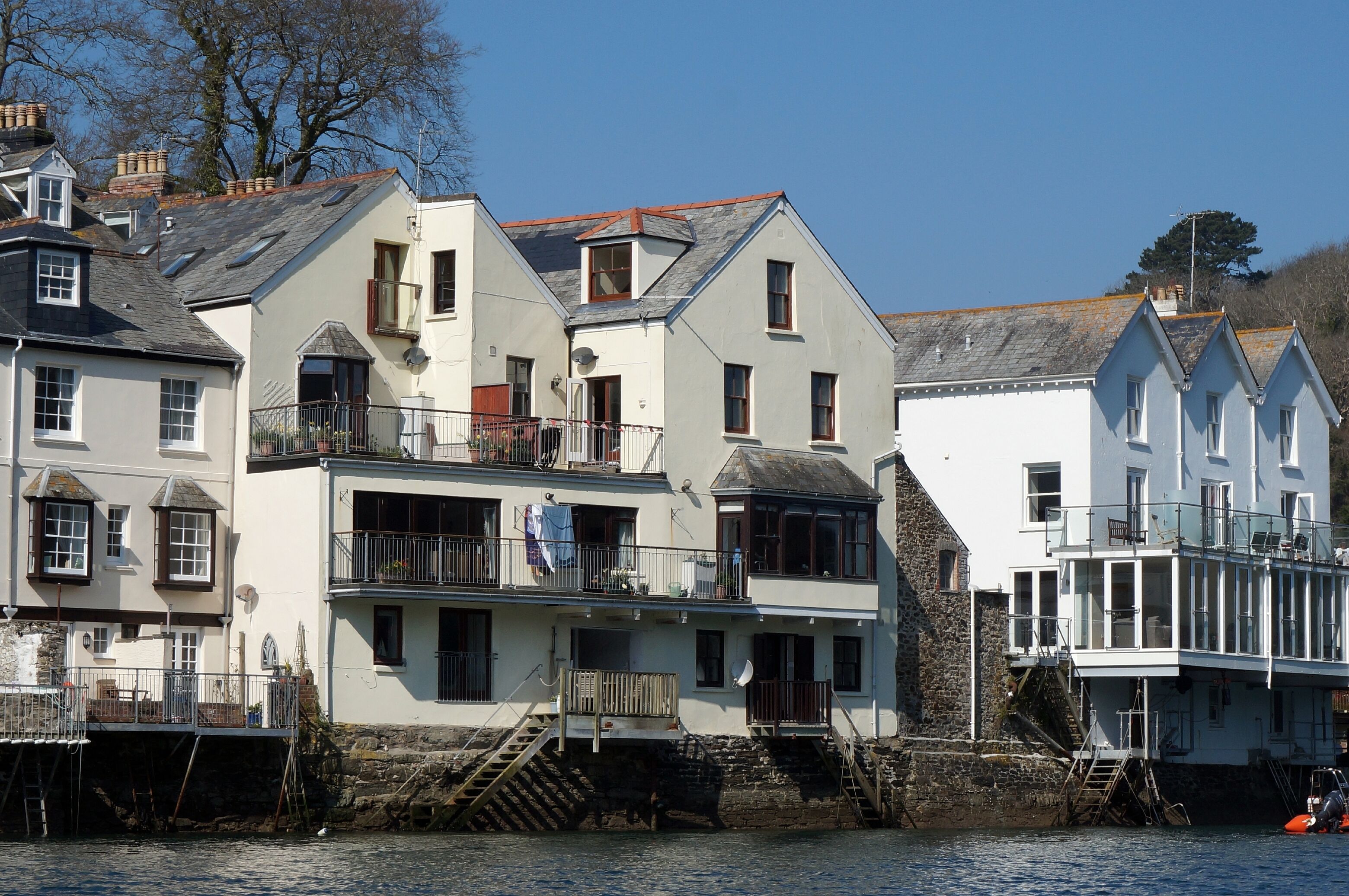 Un bâtiment situé au bord de l’eau, doté de nombreux balcons, d’un escalier menant aux étages supérieurs et d’une zone aménagée en quai.