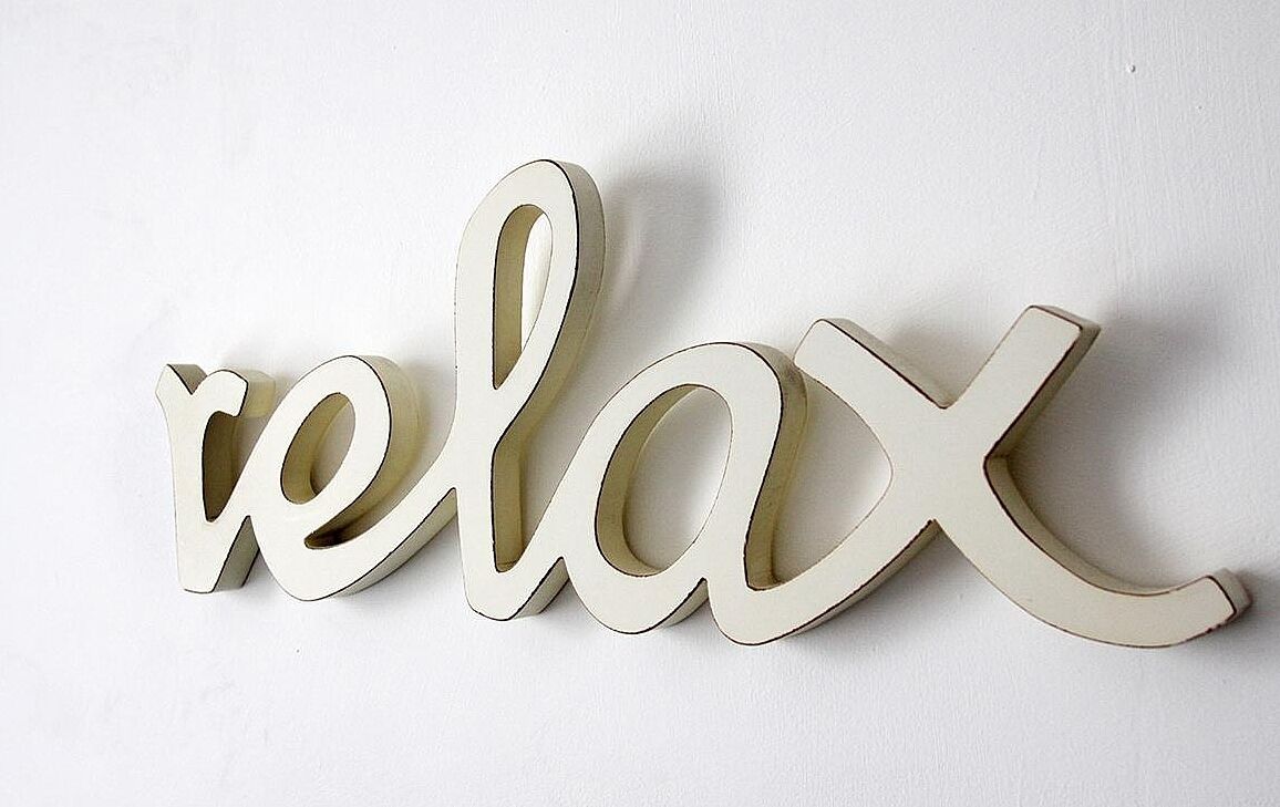 A wall-mounted sign with the word "relax" in a cursive, three-dimensional style.