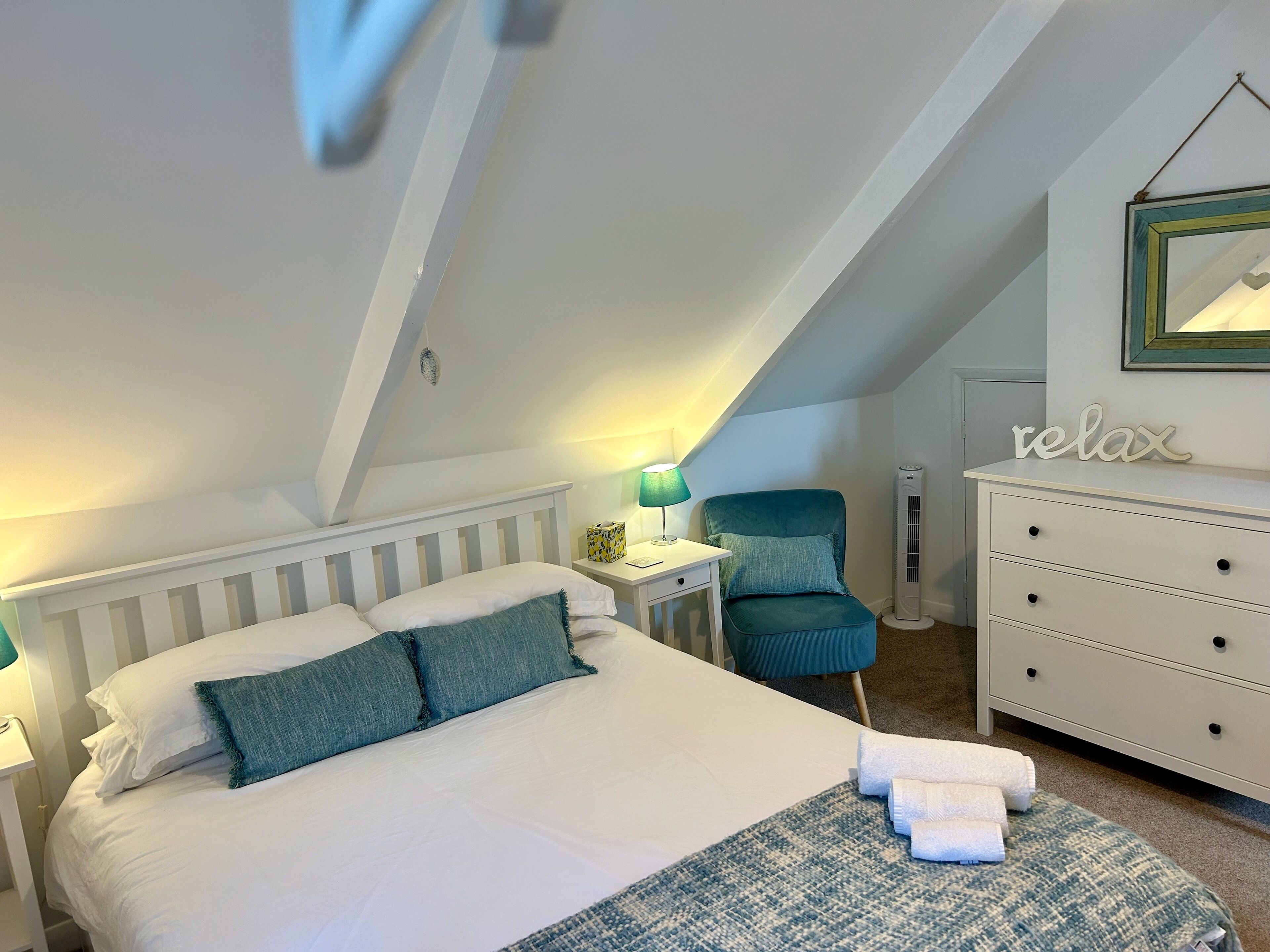 Une chambre à coucher comprenant un lit, une chaise, une commode et une table de chevet avec une lampe.