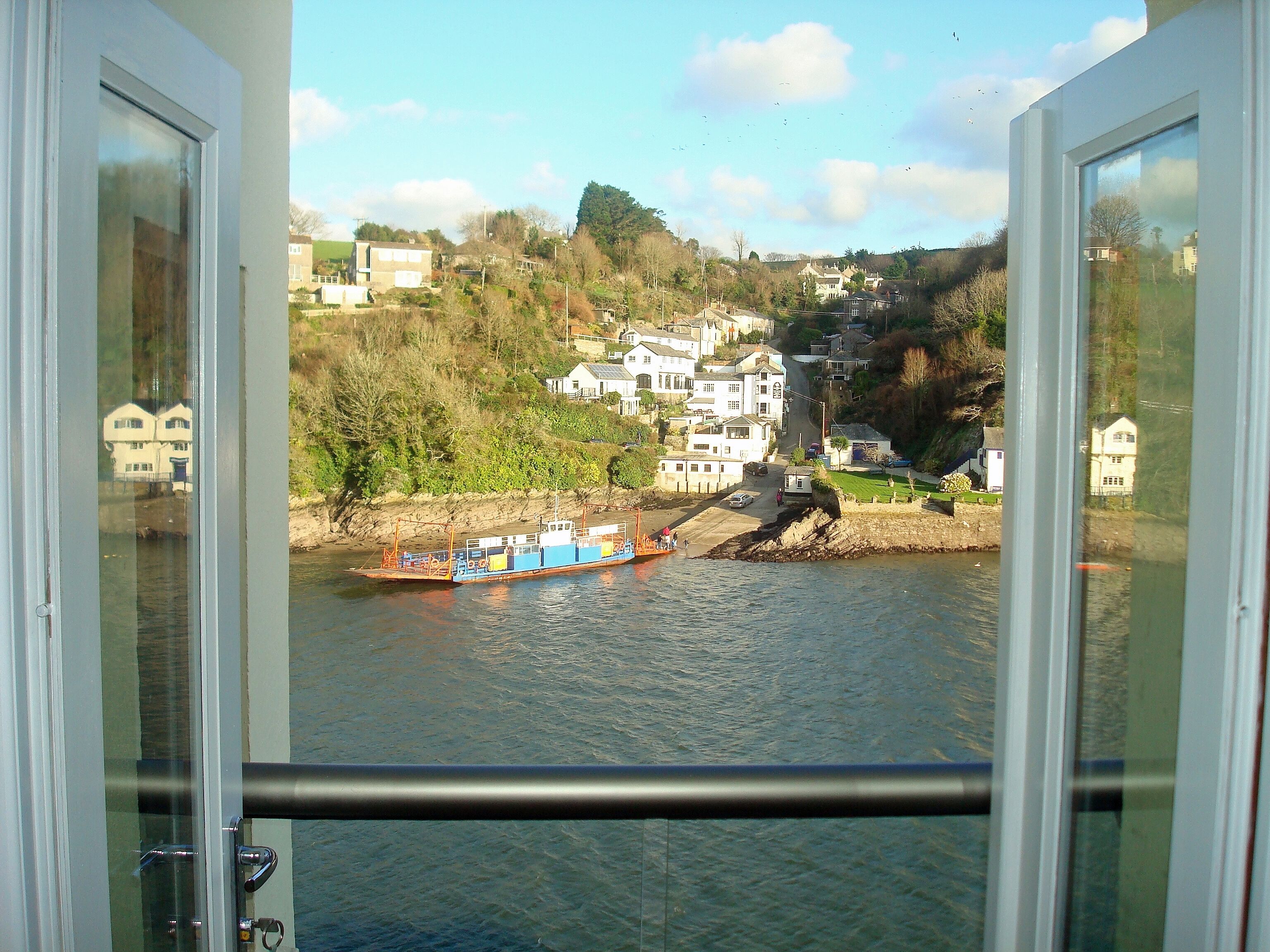 A view from a window overlooking a river with a boat, houses, and a hillside.