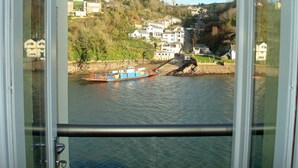 Vista desde una ventana sobre un río, con una barca, casas y una ladera.
