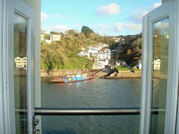 A view from a window overlooking a river with a boat, houses, and a hillside. - Waterside Holiday Home with Fantastic Views (Fowey)
