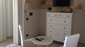 Een kamer met een plafond van natuursteen, een witte dressoir met lades, een klein rond tafeltje met een afstandsbediening en een aan de muur bevestigde televisie.