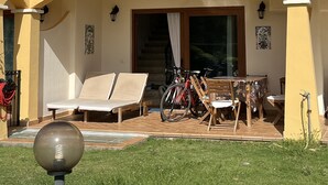 A two-story building with a yellow facade, a balcony with metal railings, and a covered patio area with outdoor furniture and bicycles.