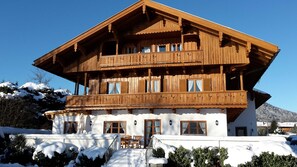 A multi-story wooden chalet with balconies, a staircase leading to the entrance, and a snow-covered landscape. - Vacation apartment 5 - Seerose am See - Dream vacation directly on Lake Tegernsee (Bad Wiessee)