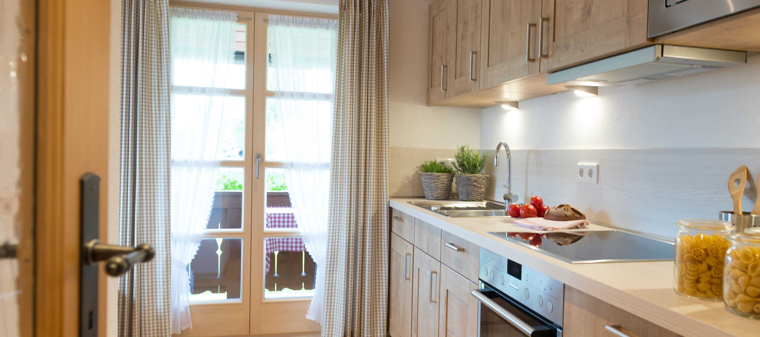 A kitchen with wooden cabinets, a stainless steel sink, a built-in oven, and a window with curtains.