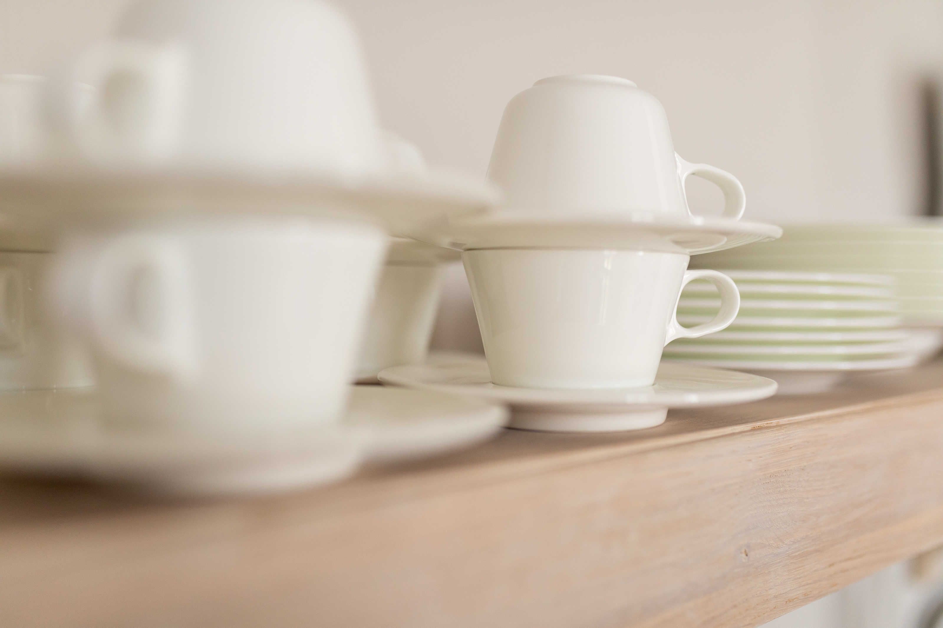 A wooden table with white ceramic cups and saucers.