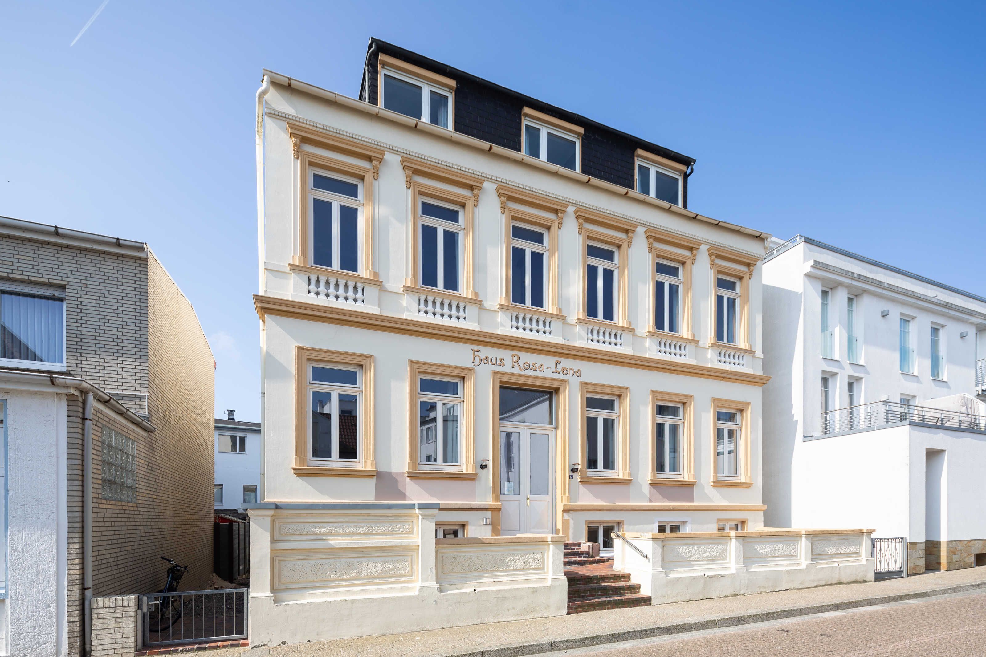 Un immeuble à plusieurs étages, de style architectural classique, qui se distingue par une entrée imposante avec des marches et un balcon.