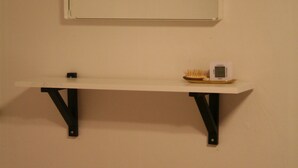 Une étagère blanche sur laquelle sont posés un petit appareil électronique et une brosse, le tout adossé à un mur uni.
