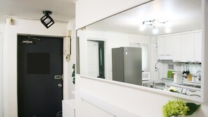 Une cuisine moderne avec des meubles blancs, une porte noire et un grand miroir qui reflète la pièce.