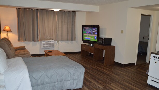 Une chambre d’hôtel comprenant un lit, un bureau avec une télévision, une lampe et une kitchenette.